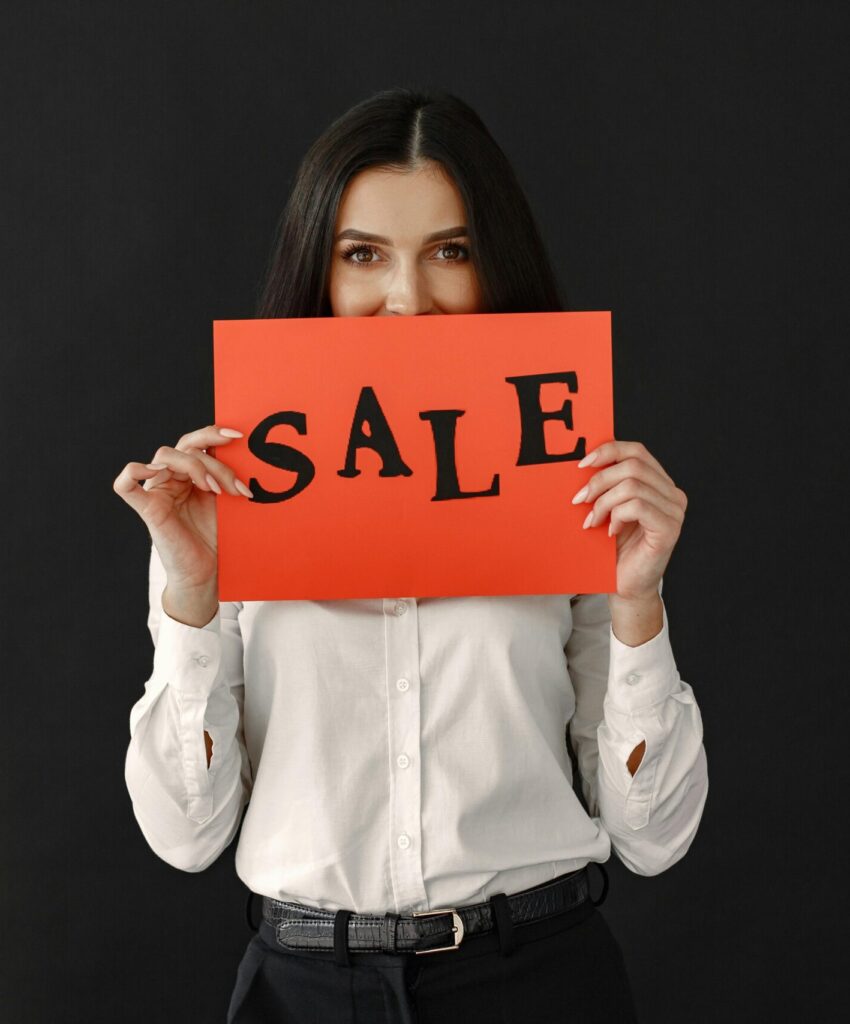 Woman in white shirt holding a red sale sign against a black backdrop. Ideal for advertising.