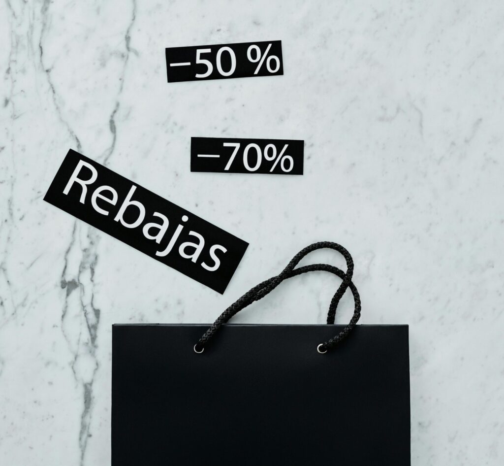 Modern flat lay featuring a black shopping bag with 50% and 70% sale tags on a marble surface.