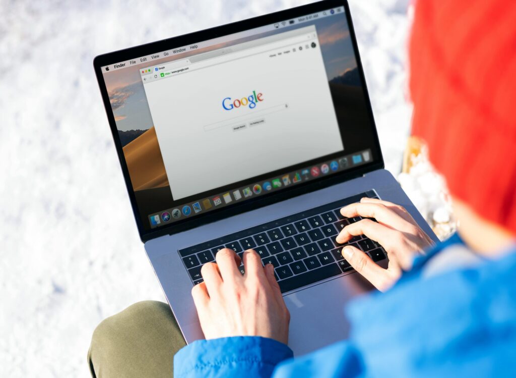 Individual typing on a laptop outdoors with snow, accessing the internet.