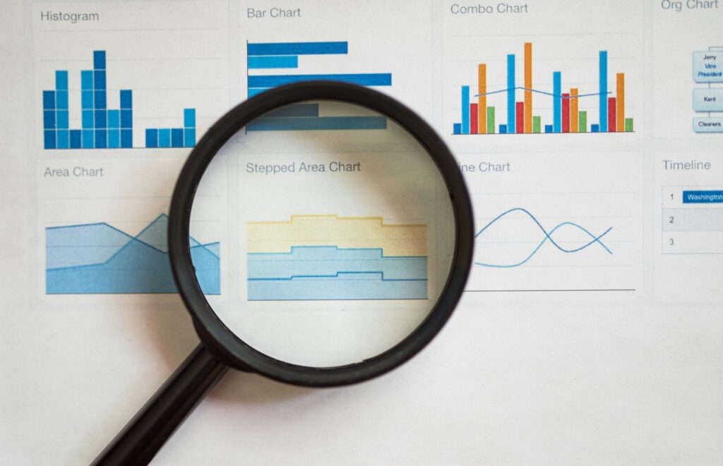 A magnifying glass focuses on various business charts and graphs on paper.